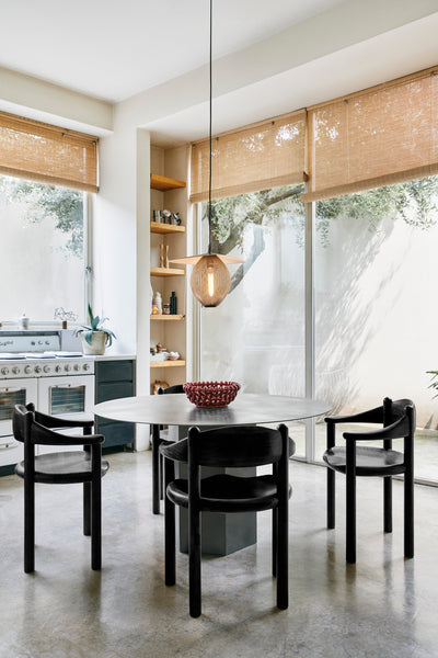Modern kitchen with a round dining table and black chairs, featuring a pendant light and large windows.