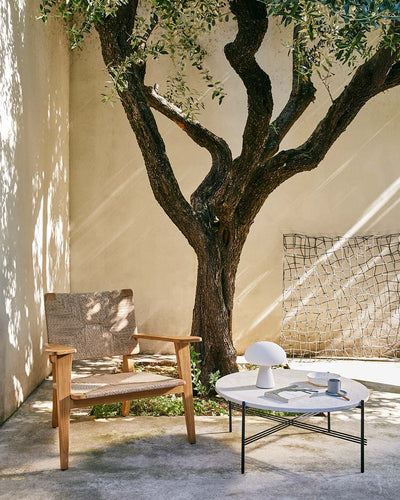 Outdoor setting with a wooden chair, round table, and tree against a beige wall.