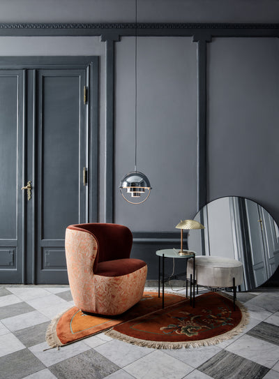 Modern interior with a brown armchair, round mirror, and decorative rug on a checkered floor.