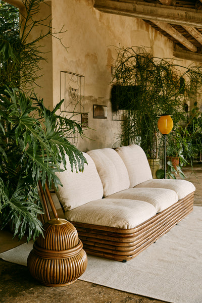 Wicker sofa in a room with plants and a textured wall.